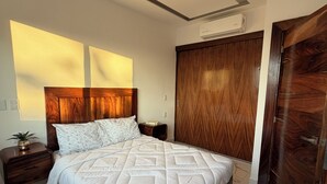 Un dormitori amb un llit gran, un armari de fusta, una nitriera i un aparell d'aire condicionat.