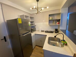A compact kitchen with a refrigerator, microwave, stove, sink, and a ceiling light fixture.