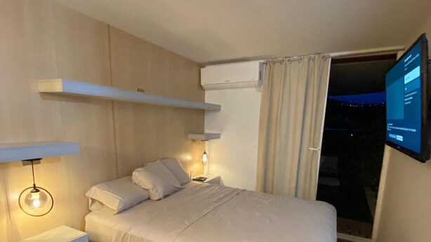 Un dormitorio moderno con una cama, mesitas de noche, un televisor montado y un equipo de aire acondicionado.