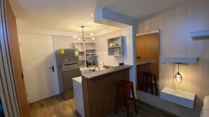 Una cocina compacta con refrigerador incorporado, detalles de madera y un pequeño comedor con taburetes.