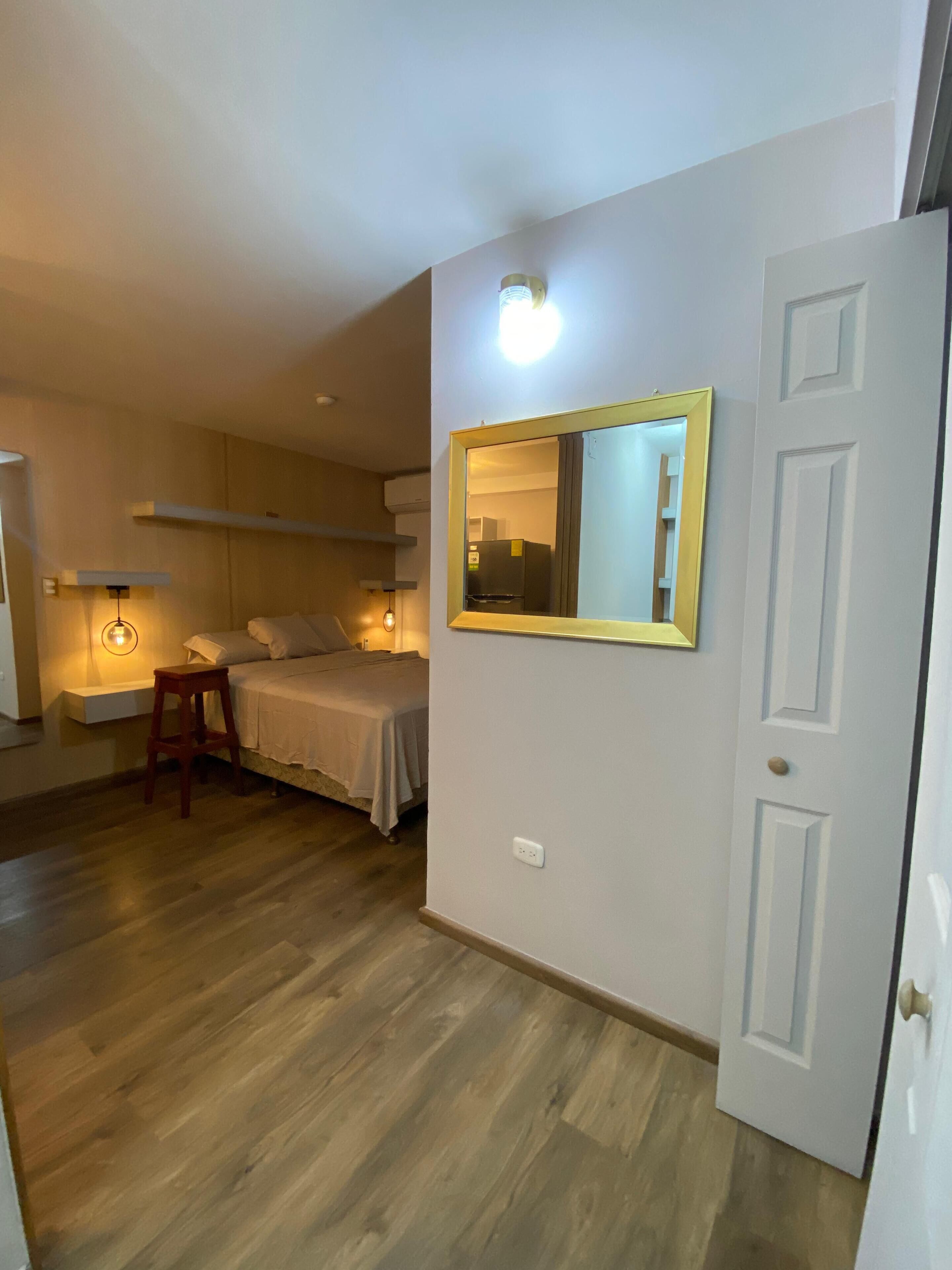 A bedroom with a bed, bedside table, chair, and a mirror on the wall.