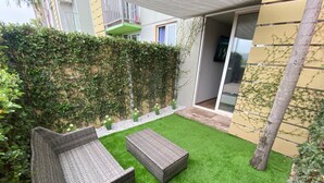 Un patio con césped artificial, dos sofás de mimbre y una pequeña mesa.