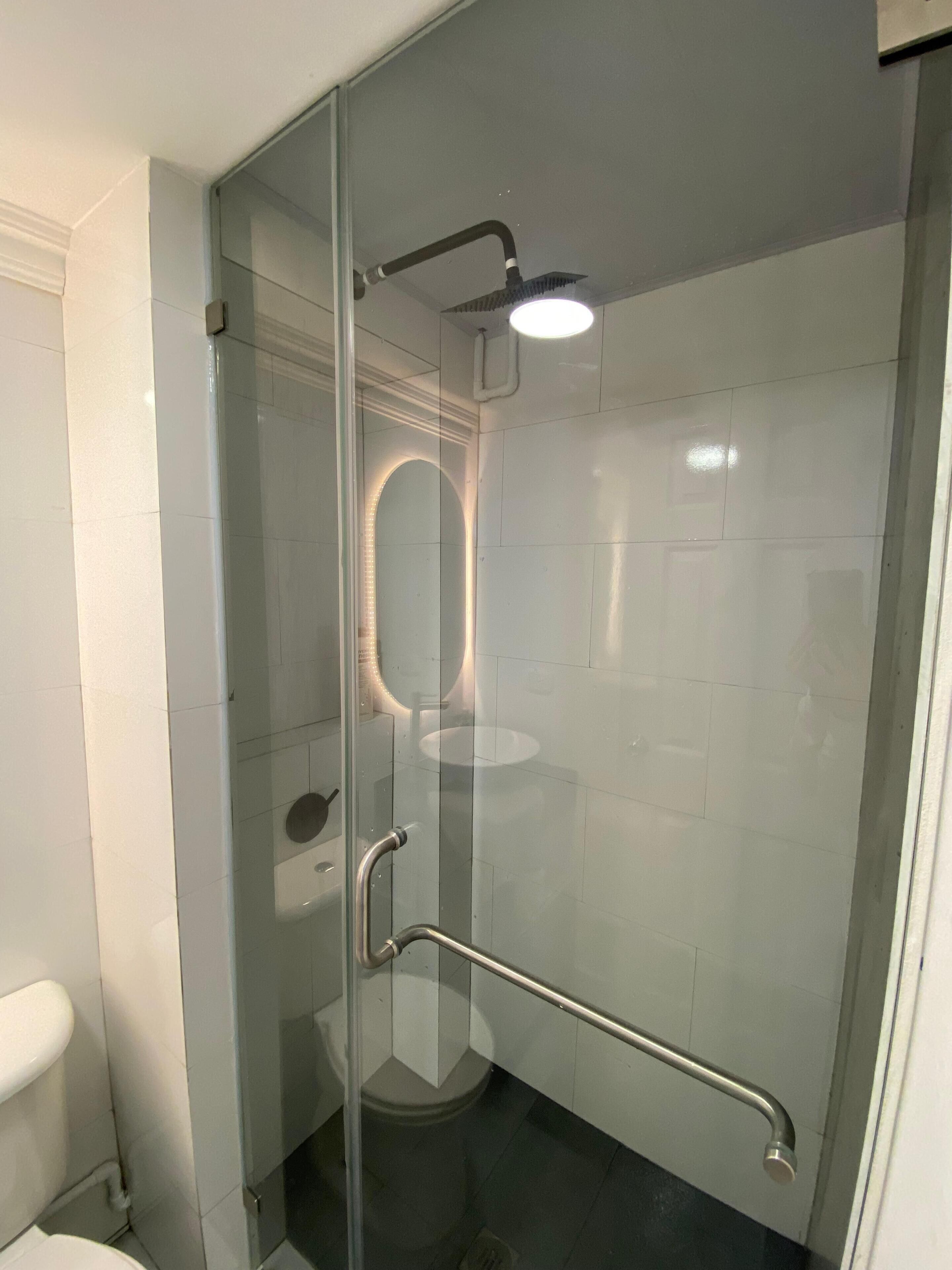 A modern bathroom with a glass shower enclosure, a glass door, and a handrail.