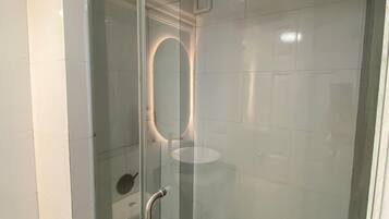 A modern bathroom with a glass shower enclosure, a glass door, and a handrail.