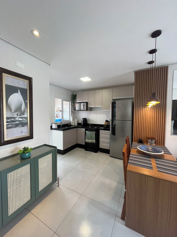 A modern kitchen with a dining area, featuring a large island, built-in appliances, and a pendant light. - Wonderful apartment 50 meters from the beach. (Bertioga)
