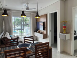 A modern living room with a dining area, a TV mounted on the wall, and a view of the outdoors. - Wonderful apartment 50 meters from the beach. (Bertioga)