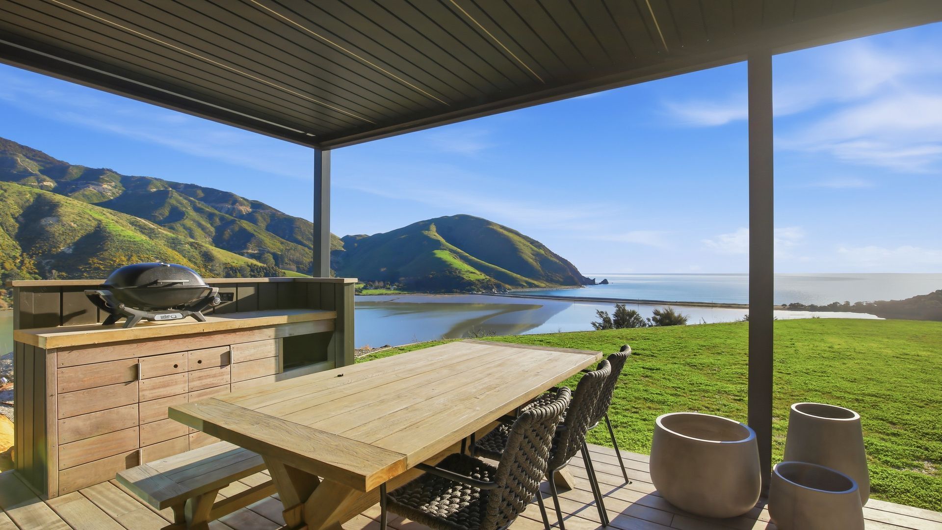 An outdoor patio with a wooden table, a grill, and a view of a lake and mountains.