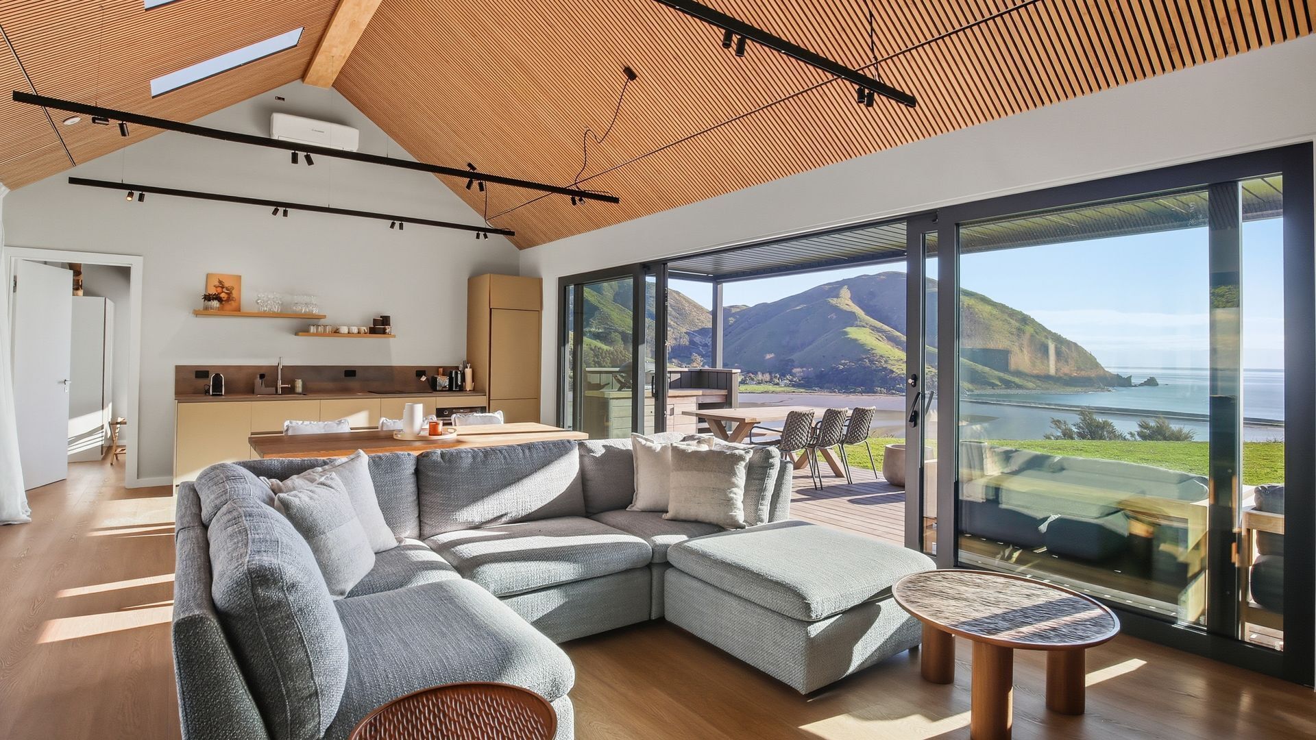 A modern living room with a large sectional sofa, a small round table, and a view of the ocean.