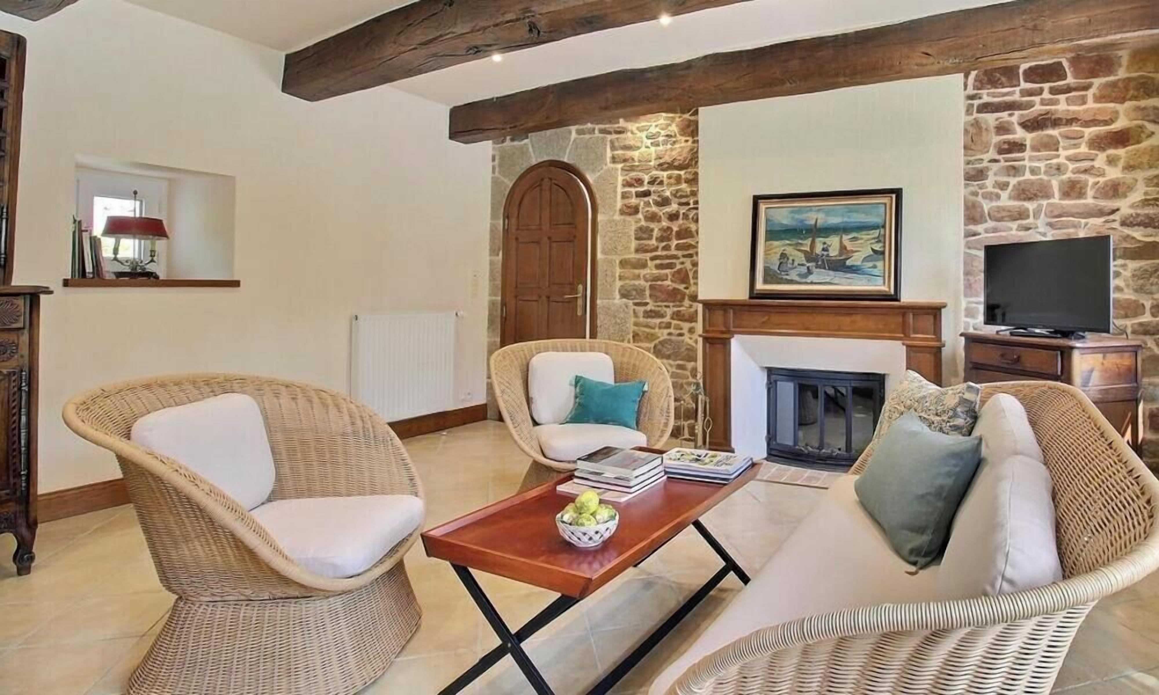 Una sala de estar con muebles de mimbre, una chimenea, una pared de piedra y un televisor.