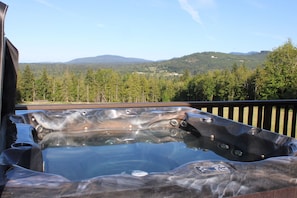 A hot tub on a deck with a view of a forested mountain range.