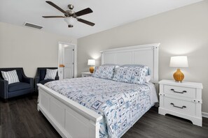 A bedroom with a bed, two nightstands, a chair, a ceiling fan, and a door.
