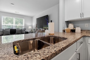 A modern kitchen with granite countertops, stainless steel sinks, and white cabinetry.