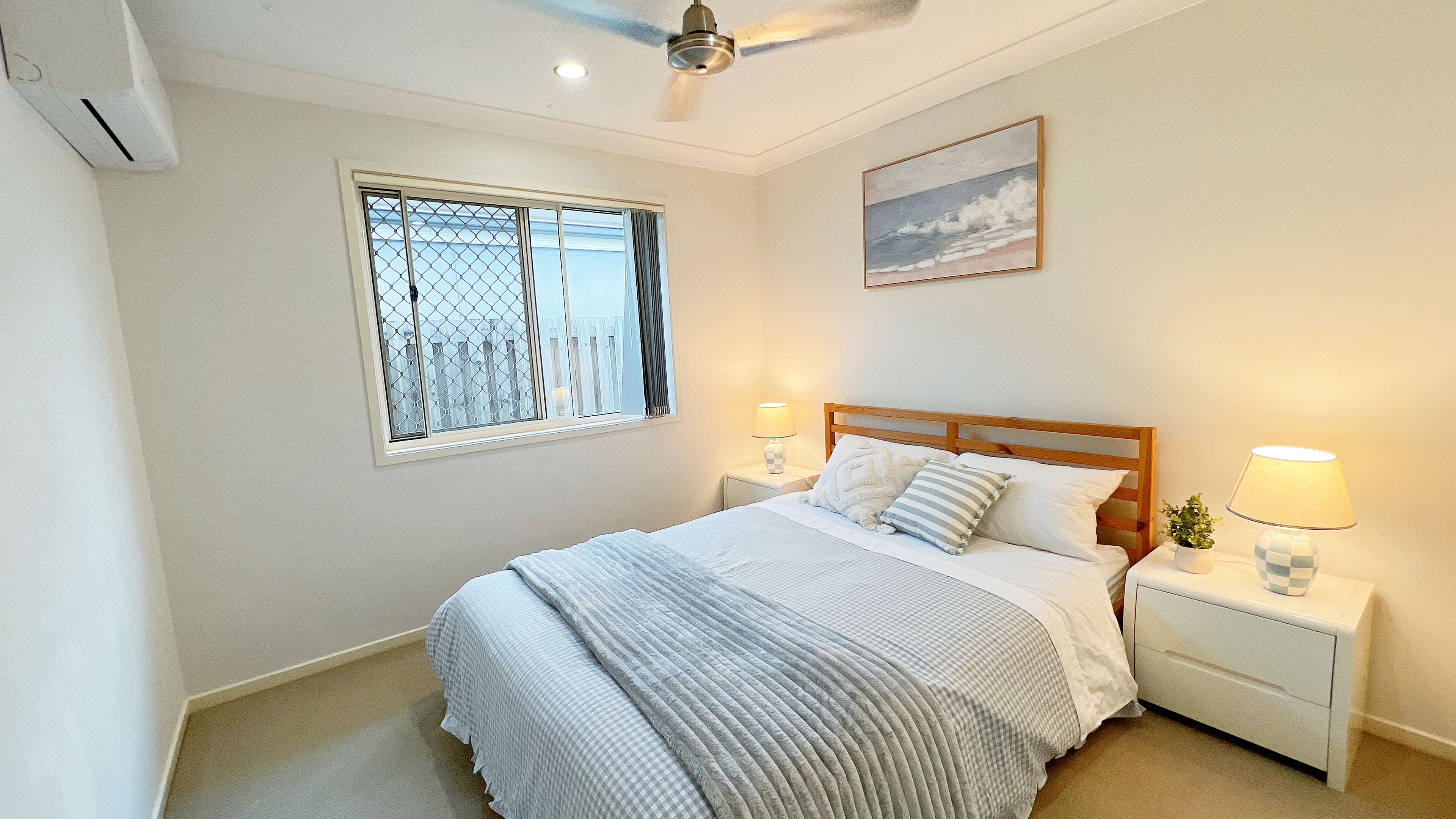 Ein Schlafzimmer mit einem Bett, zwei Nachttischlampen, einem Deckenventilator, einem Fenster mit Vorhängen und einem Bild an der Wand.