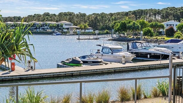 A marina with boats docked, a dock, and a view of houses and trees in the background. - Peaceful Oasis, Prime Location - close to Pool, Gym, and Golf Courses (Hope Island)