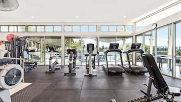 Une salle de sport équipée de tapis de course, d’appareils de musculation et d’un ventilateur.