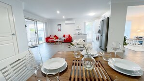 A modern kitchen with a refrigerator, a dining table set with plates and glasses, and a red sofa in the background. - Peaceful Oasis, Prime Location - close to Pool, Gym, and Golf Courses (Hope Island)
