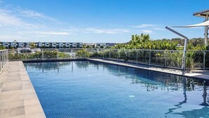 A swimming pool with a clear blue water surface, surrounded by a tiled deck and a metal railing. - Peaceful Oasis, Prime Location - close to Pool, Gym, and Golf Courses (Hope Island)