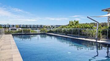 A swimming pool with a clear blue water surface, surrounded by a tiled deck and a metal railing.