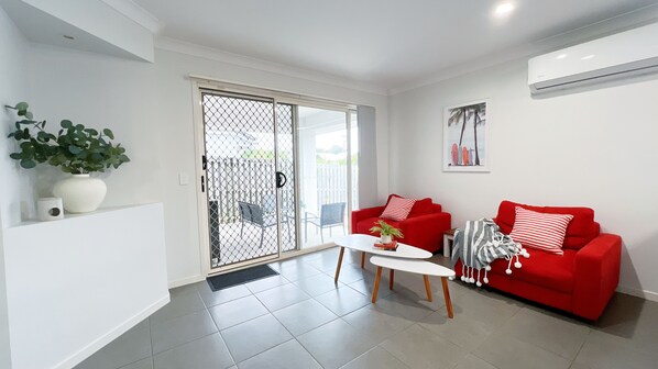 A living room with a red sofa, a white coffee table, and a sliding glass door leading to an outdoor area.