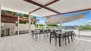 An outdoor patio with a grill, tables, and chairs, overlooking a body of water. - Peaceful Oasis, Prime Location - close to Pool, Gym, and Golf Courses (Hope Island)