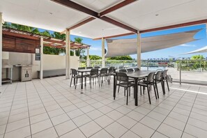 An outdoor patio with a grill, tables, and chairs, overlooking a body of water. - Peaceful Oasis, Prime Location - close to Pool, Gym, and Golf Courses (Hope Island)