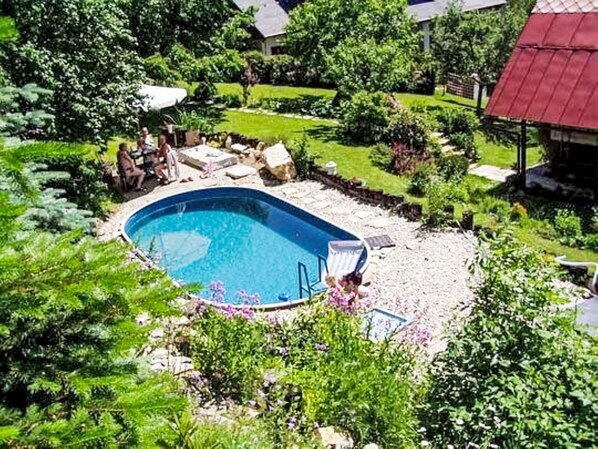 Une piscine entourée d’une végétation luxuriante et un bâtiment dont le toit est de couleur rouge.