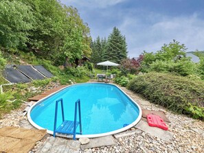 Une piscine avec une terrasse en bois, une échelle et un flotteur rouge.