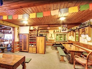 A cozy bar area with wooden furniture, shelves of bottles, and a wooden ceiling with colorful flags. - Apartment Černý by Interhome (Rokytnice nad Jizerou)