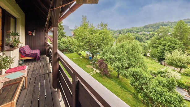 A wooden balcony with a view of a lush green landscape and a distant village. - Apartment Černý by Interhome (Rokytnice nad Jizerou)