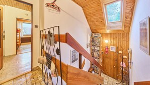A wooden staircase with a metal railing, a wooden ceiling, and a bookshelf with books and decorative items. - Apartment Černý by Interhome (Rokytnice nad Jizerou)