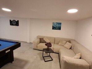 Ein Wohnzimmer mit Billardtisch, einem beigefarbenen Sofa, einem kleinen Tisch mit einer Vase und zwei Wanddekorationen.