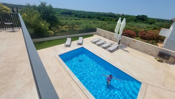Ein Pool auf dem Dach mit Liegestühlen und Sonnenschirmen, umgeben von Grün und mit freiem Blick auf die Landschaft.