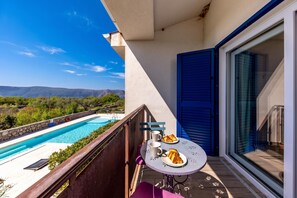 A balcony with a pool, a table with a plate of croissants, and a view of the mountains. - Wabi Sabi Apt8 Pool & Sea View, Brzac, Croatia (Brzac)