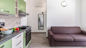 A modern kitchen with green cabinets, a stove, and a dining area with a brown sofa. - Wabi Sabi Apt8 Pool & Sea View, Brzac, Croatia (Brzac)