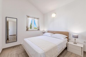 A bedroom with a bed, bedside tables, a nightstand, a mirror, a window with curtains, and a wall-mounted light fixture. - Wabi Sabi Apt7 Pool & Sea View, Brzac, Croatia (Brzac)