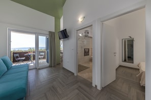 Ein modernes Zimmer mit Fischgrätparkett, einer Couch, einem an der Wand montierten Fernseher und einer Schiebetür zu einem Außenbereich mit Tisch und Stühlen.