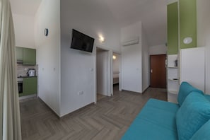Ein kleines Hotelzimmer mit einer Küchenzeile, einem Flachbildfernseher, einem Bett und einer Wand in Grünton.