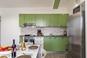 A modern kitchen with green cabinets, a stainless steel refrigerator, and a dining area with a table set for two.
