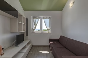 Ein modernes Zimmer mit Flachbildfernseher, einer Sitzecke, einem Fenster mit Vorhängen und Einbauschränken.
