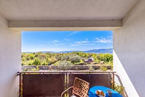 A balcony with a view of a mountainous landscape, a table with a chair, and a plate with croissants. - Wabi Sabi Apt3 Pool & Sea View, Brzac, Croatia (Brzac)