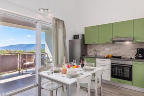 A modern kitchen with green cabinets, a dining table set for two, and a view of the mountains through the sliding glass door. - Wabi Sabi Apt3 Pool & Sea View, Brzac, Croatia (Brzac)
