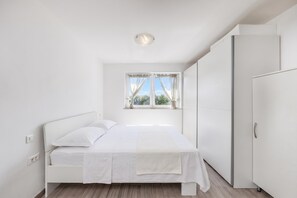 A minimalist bedroom with a single bed, a wardrobe, and a window with curtains. - Wabi Sabi Apt6 Pool & Garden, Brzac, Croatia (Brzac)