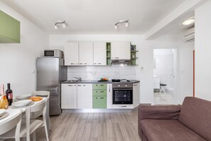 Une cuisine compacte équipée d’un réfrigérateur, d’un four à micro-ondes, d’une cuisinière et d’un four. On y trouve également un coin repas avec une table et des chaises, ainsi qu’un canapé marron.