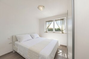 Ein Schlafzimmer mit einem Bett, einem Fenster mit Vorhängen, einer Deckenleuchte und einer Steckdose.