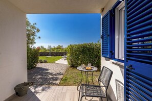 A patio with a table and chairs, a bucket, and a view of a garden and street. - Wabi Sabi Apt5 Pool & Garden, Brzac, Croatia (Brzac)
