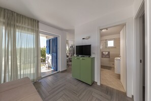 A modern living room with a sofa, a television on a cabinet, and a sliding glass door leading to an outdoor area. - Wabi Sabi Apt5 Pool & Garden, Brzac, Croatia (Brzac)