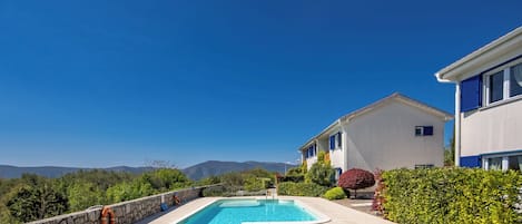 Piscina com espreguiçadeiras, um muro de pedra e vista para montanhas.