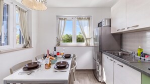 Een moderne keuken met een eetgedeelte, roestvrijstalen apparatuur en uitzicht op groen.
