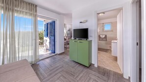 Een moderne woonkamer met een bank, een televisie op een kast, en een glazen schuindeur naar een balkon.