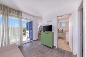Ein modernes Wohnzimmer mit einer Couch, einem Fernseher auf einem Schrank und einer Glastür, die auf einen Balkon führt.